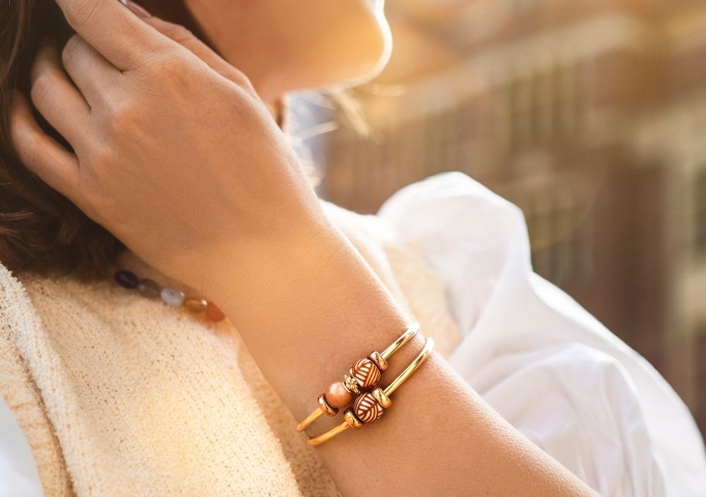 Nærbillede af to forgyldte bangles stylet med kugler i sommerens sollys.
