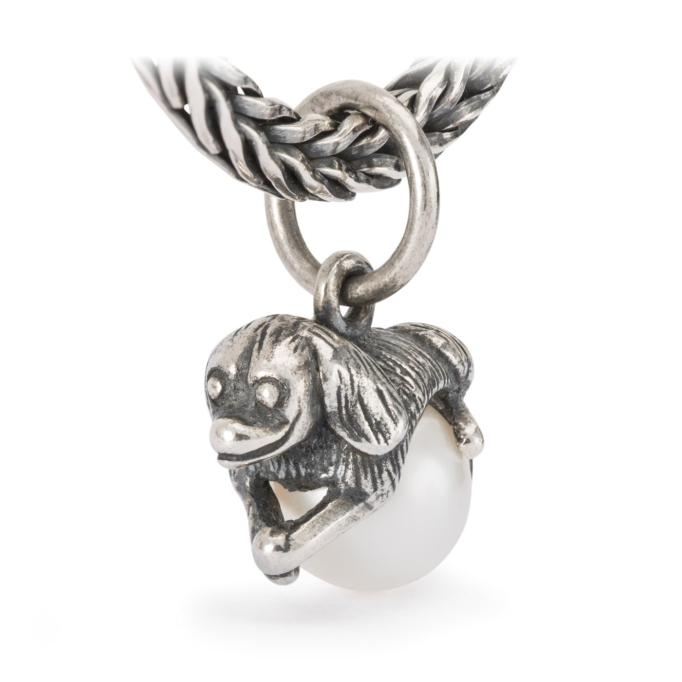 Jewellery silver pendant of a dog laying on a white pearl.